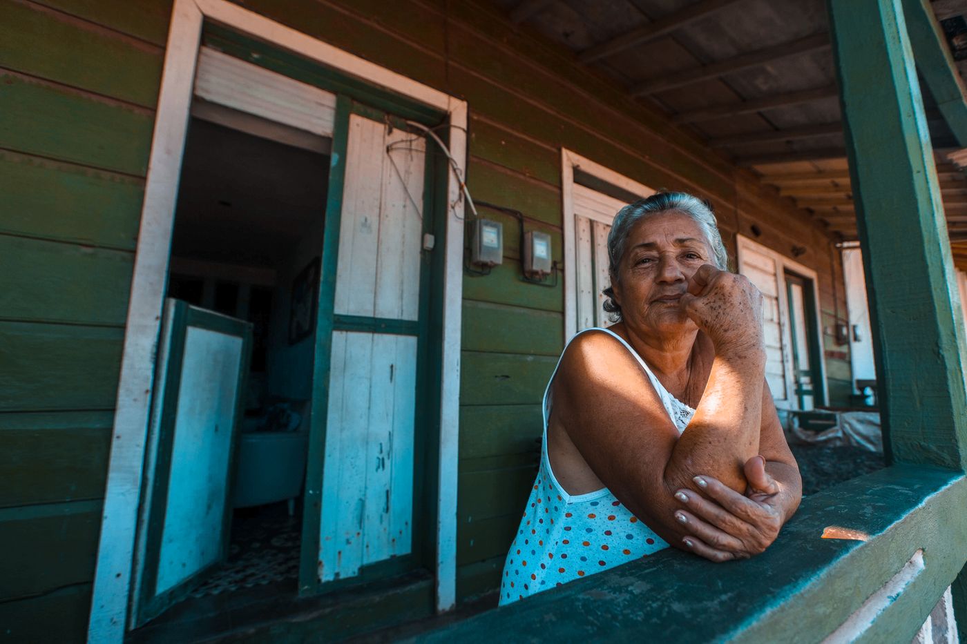 A woman resting her hands on the wooden railing of a porch.